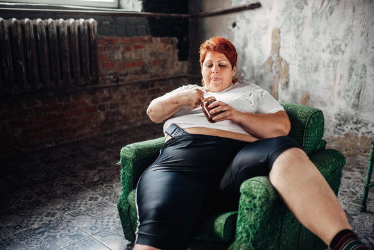 Overweight woman sits in a chair and eats sweets
