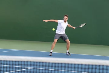  Professional tennis player athlete man focused on hitting ball over net on hard court playing tennis match with someone. Sport game fitness lifestyle person living an active summer lifestyle. © Maridav