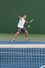 Professional tennis player athlete man hitting forehand ball over net on hard court playing tennis match. Sport game fitness lifestyle.