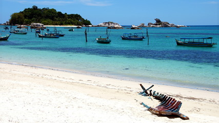 viele kleine Fischerboote ankern vor weißem Sandstrand im blauen Meer mit Insel und Felsen