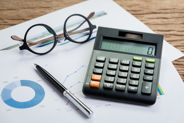 Accounting equipments, work corporate profit or finance calculations, savings concept with pen, calculator and eyeglasses on graph and pile chart paper, KPI or client campaign analysis