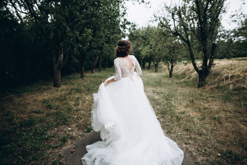 Bride in a very beautiful wedding dress is walking around the garden on her wedding day