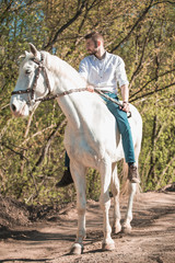 Handsome man in a shirt riding on a brown horse