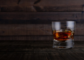 Glass of whiskey with ice cubes on wooden table