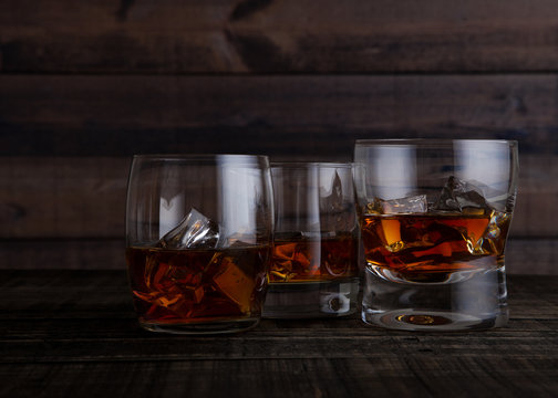 Glasses of whiskey with ice cubes on wooden table