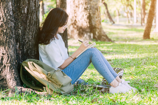 Woman with pen writing on a notebook sitting near the tree in park