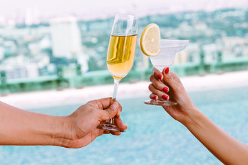 Hand of couple drinking cocktails in the swimming pool