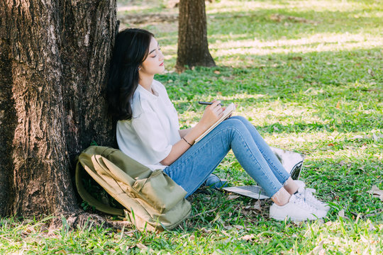 Woman with pen writing on a notebook sitting on grass in park