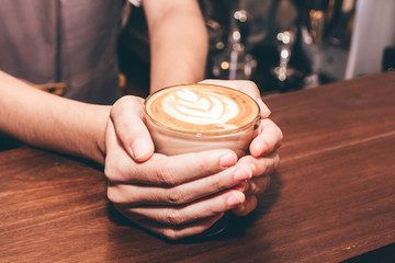 Woman barista holding coffee latte art on wooden table in coffee shop
