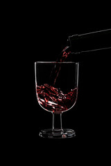A low glass of red wine is pouring wine from a bottle of red .