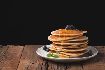 Pancakes with blueberries and honey on a wooden rustic table. Dessert for Breakfast on a black background. Copy space for your text
