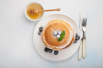 A stack of delicious pancakes with honey and blueberries on a light blue background. Top view with copy space