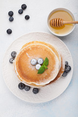 A stack of delicious pancakes with honey and blueberries on a light blue background