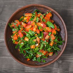 Salad of red bell pepper with herbs in a clay bowl on a wooden table.