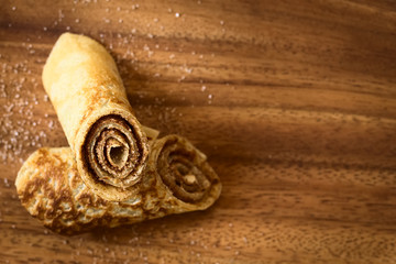 Fototapeta na wymiar Crepe rolls filled with cinnamon and sugar, photographed overhead on wood with natural light (Selective Focus, Focus on the front of the upper roll)