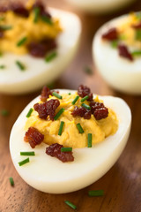 Deviled egg with bacon and chives, photographed with natural light (Selective Focus, Focus on the front of the egg yolk of the first egg)