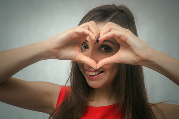 Love heart. Girl is holding hands in the shape of heart and is looking through it.