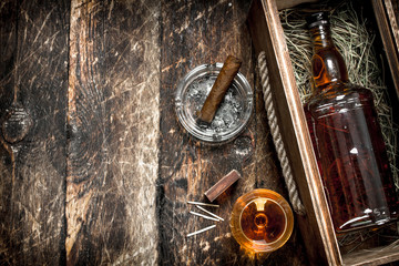 Cognac background. A bottle of cognac in a box with a glass and a cigar.