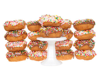 Cake donuts frosted with chocolate and vanilla frosting, rainbow candy sprinkles, stacked behind a small white pedestal with two donuts stack on top.