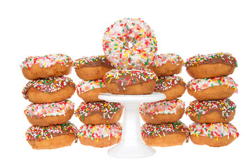 Cake donuts frosted with chocolate and vanilla frosting, rainbow candy sprinkles, stacked behind a small white pedestal with two donuts stack on top.