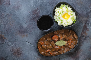 Irish beer and beef stew with champ, traditional dishes for Saint Patrick’s Day. Top view on a grey textured background with copyspace, horizontal shot
