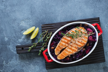 Bowl with grilled salmon on a bed of red cabbage, view from above on a blue stone background with space, horizontal shot