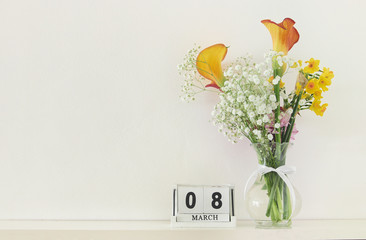 International women day concept with beautiful flowers in the vase and date on wooden table.