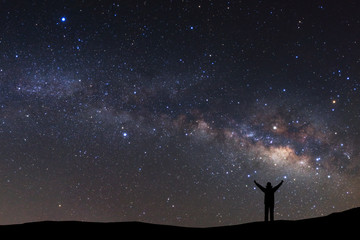 Fototapeta na wymiar landscape with milky way, Night sky with stars and silhouette of a standing sporty man with raised up arms on high mountain.