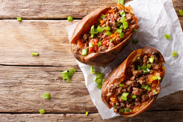 Baked sweet potatoes stuffed with ground beef with tomatoes and onions on paper. horizontal top view
