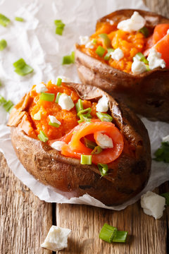 baked sweet potato stuffed with salmon, feta cheese and green onion close-up on parchment. vertical