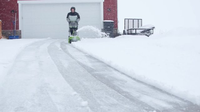 A man snowblowing his driveway during the blizzard
