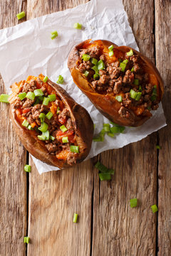 Organic food: baked sweet potato stuffed with ground beef and green onion close-up on paper. Vertical top view