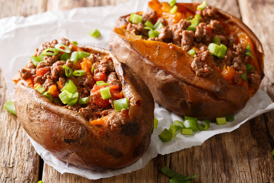 Homemade baked sweet potato stuffed with beef meat and green onions close-up on the table. horizontal
