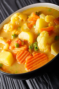 Vegetarian curry from potatoes, carrots, cauliflower, peas, tomatoes close-up in a bowl on the table. vertical