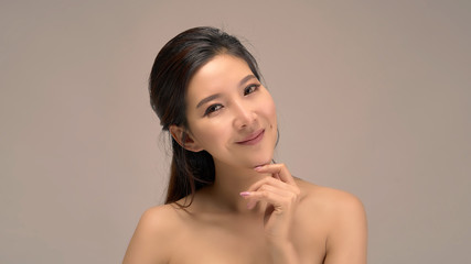 Happy beautiful asian girl with the fresh skin in grey colour background. Expressive facial expressions. Cosmetology and Spa concept.