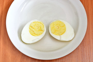 Half hard boiled chicken egg on a white saucer and wooden table