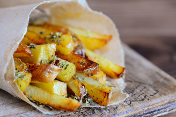 Homemade spicy fries in paper and on a wooden board. Potato recipe for dinner or lunch. Closeup