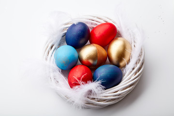 Eggs painted in various colors arranged with feathers in twig wreath on white background. Easter traditions concept.