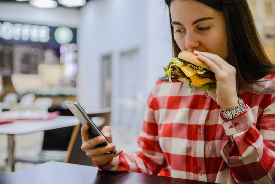 woman eat humburger while searfing the phone