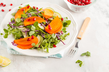 Persimmon salad with pea leaves, cucumber and pomegranate in white plate. Healthy vegetarian food concept. Copy space