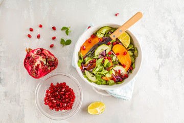 Persimmon salad with pea leaves, cucumber and pomegranate in white bowl. Healthy vegetarian food concept. Top view, copy space.