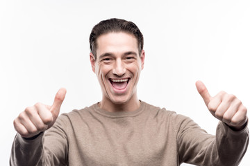 Fototapeta premium Everything is perfect. Upbeat young man showing thumbs up and grinning while being isolated on the white background