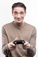 Diligent player. Cheerful handsome man holding a video game controller and widening his eyes, playing enthusiastically