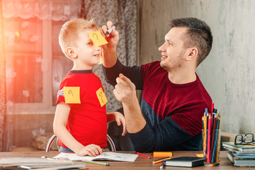 The father and his little son fool around doing homework for the school.