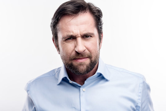 Full of negative. Angry middle-aged man in a baby blue shirt staring at the camera with an expression of irritation while posing against a white background