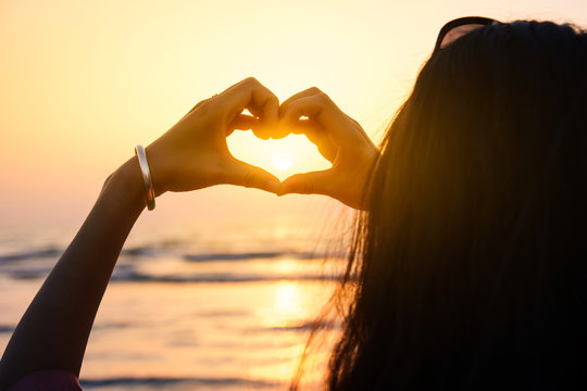Girl making heart shape with hands in the sunset