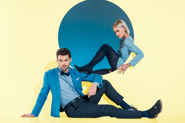 attractive stylish couple sitting and looking at camera on yellow