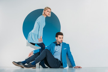 attractive stylish couple sitting and looking at camera on grey