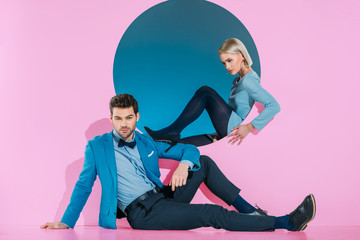 attractive stylish couple sitting and looking at camera on pink