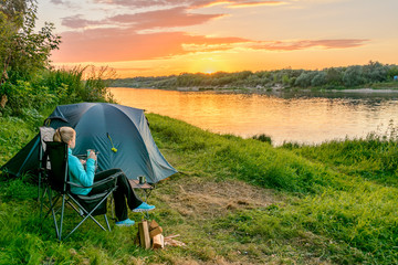 Young woman in camping with a tourist tent on the river bank. Russia.